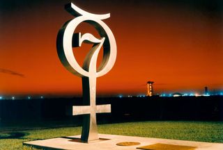 photo of a monument, featuring the number 7, at sunrise, with an orange sky behind it