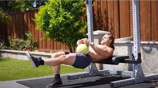 Marcus Filly performing a one-legged kettlebell hip thrust in a garden using a bench