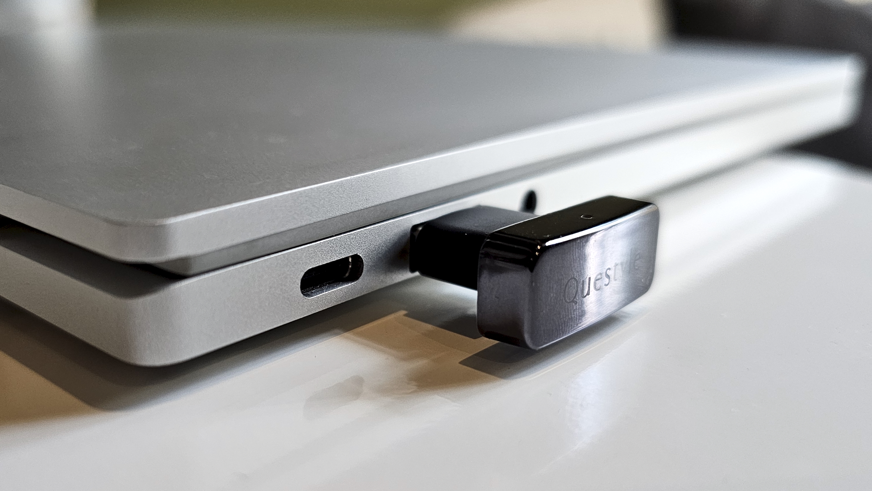 The Questyle QCC Dongle Pro with a smartphone to denote size, on a light wooden table