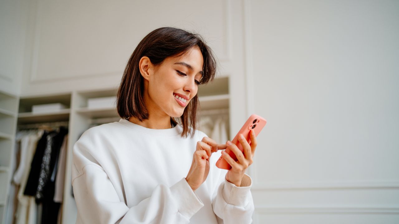 A smiling caucasian woman shopping the Presidents&#039; Day sales on her iphone smartphone