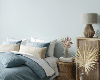 a blue boho bedroom with blue walls and comforter and a small table as a nightstand with flowers on it