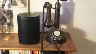 A Sonos One speaker on a wooden surface next to an old-fashioned telephone