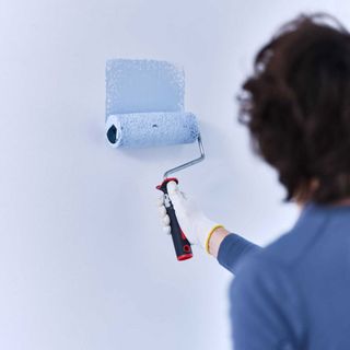 person painting blue wall with a roller