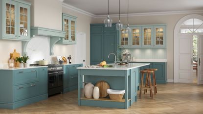 A blue/light blue kitchen with a large island in the middle as well as upper and lower cabinets. The upper cabinets have glass fronted doors, while the lower cabinets are closed off