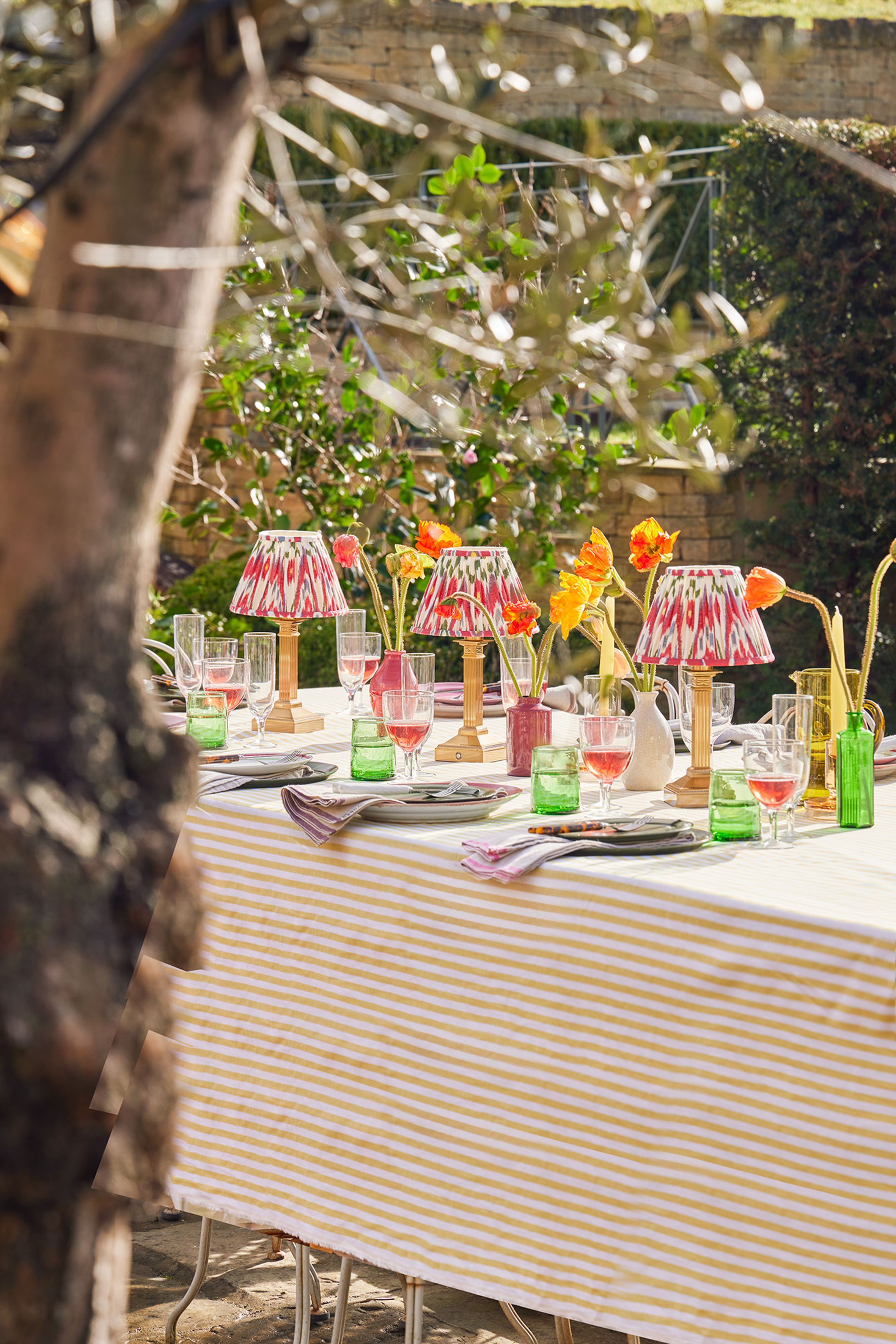 An outdoor table setting with a striped tablecloth and three lamps as centerpieces
