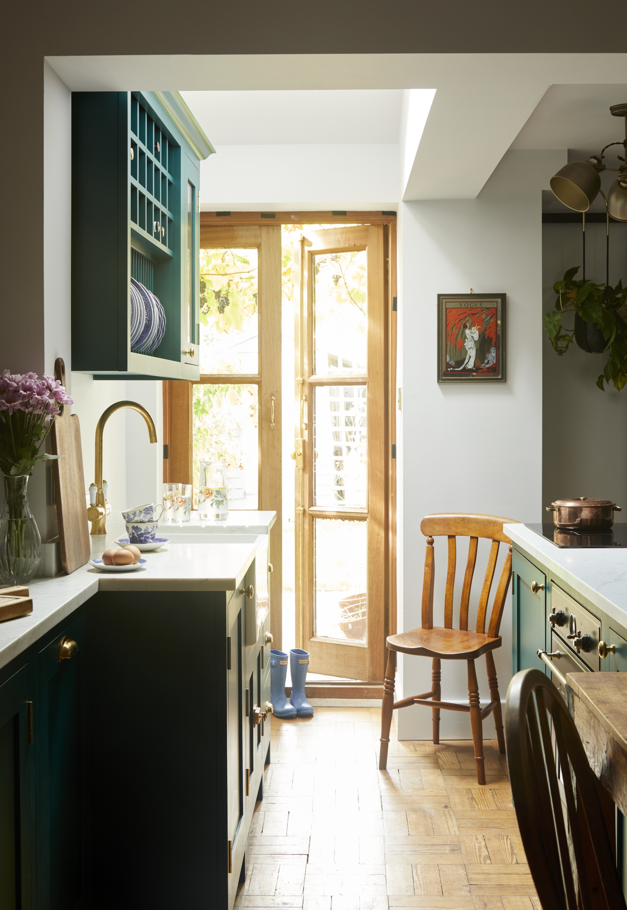 A narrow but homely teal kitchen with open shelving and brass accents and french doors at the back