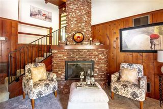 A dated living area with a brick fireplace, two patterned armchairs, and wood panelled walls