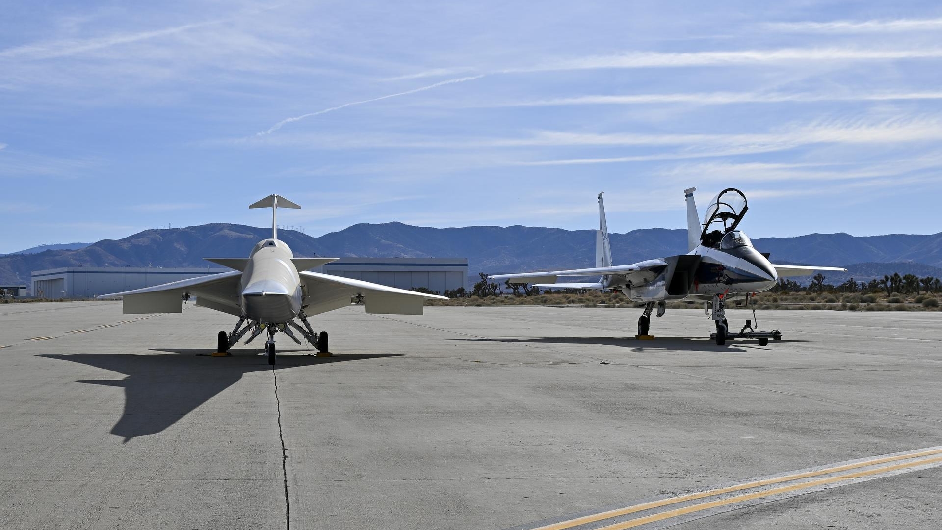 two sleek, small jets sit on a concrete tarmac in the desert