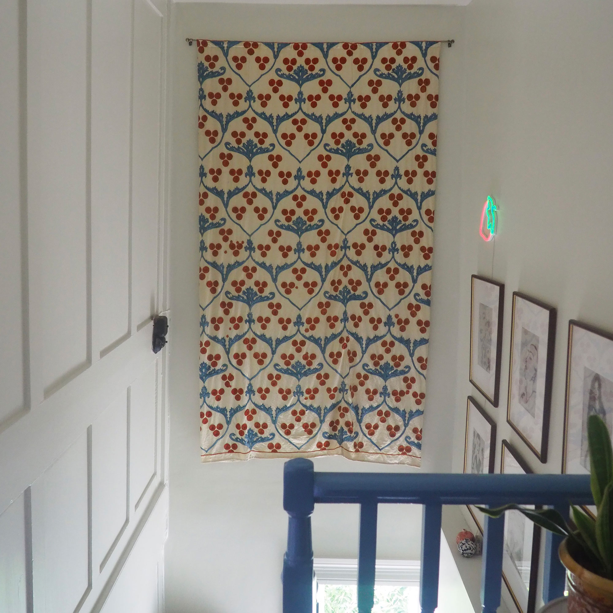 Colourful patterned wall hanging in ceiling area above staircase with blue banisters, beside gallery wall