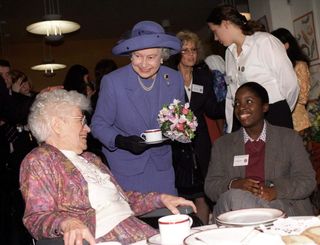 Queen Elizabeth holding a teacup and talking to two people