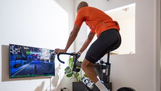 A black man in an orange jersey on an indoor bike using a virtual cycling platform