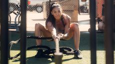 Hannah Eden, CrossFit athlete, pulls a heavy weight on a rope towards herself, while holding a squat position.