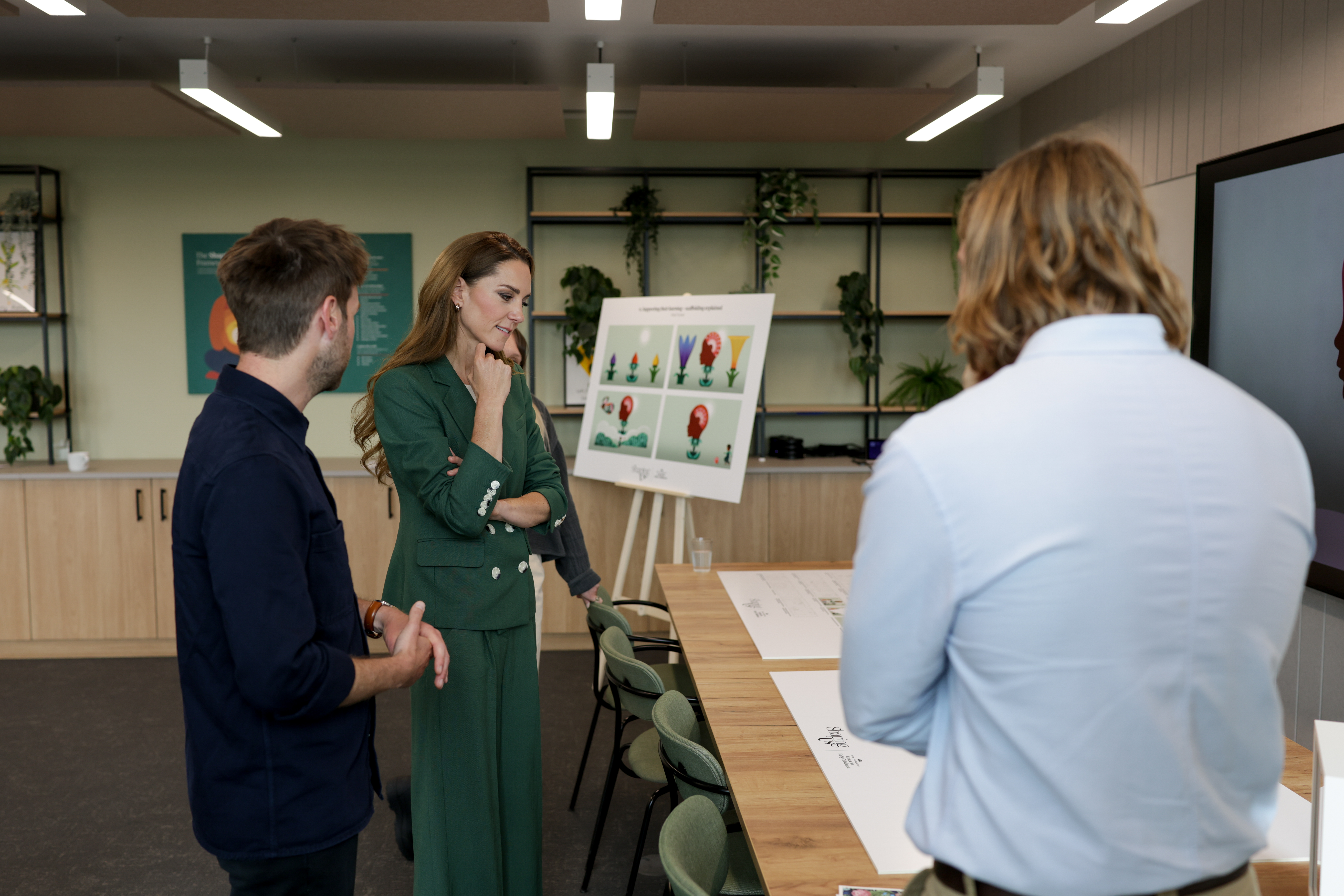 Kate Middleton wearing a green suit and resting her chin on her hand looking at drawings on a table
