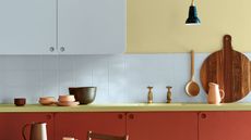 modern kitchen worktop with pale yellow wall, white upper cabinets and white backsplash, dark red lower cabinets