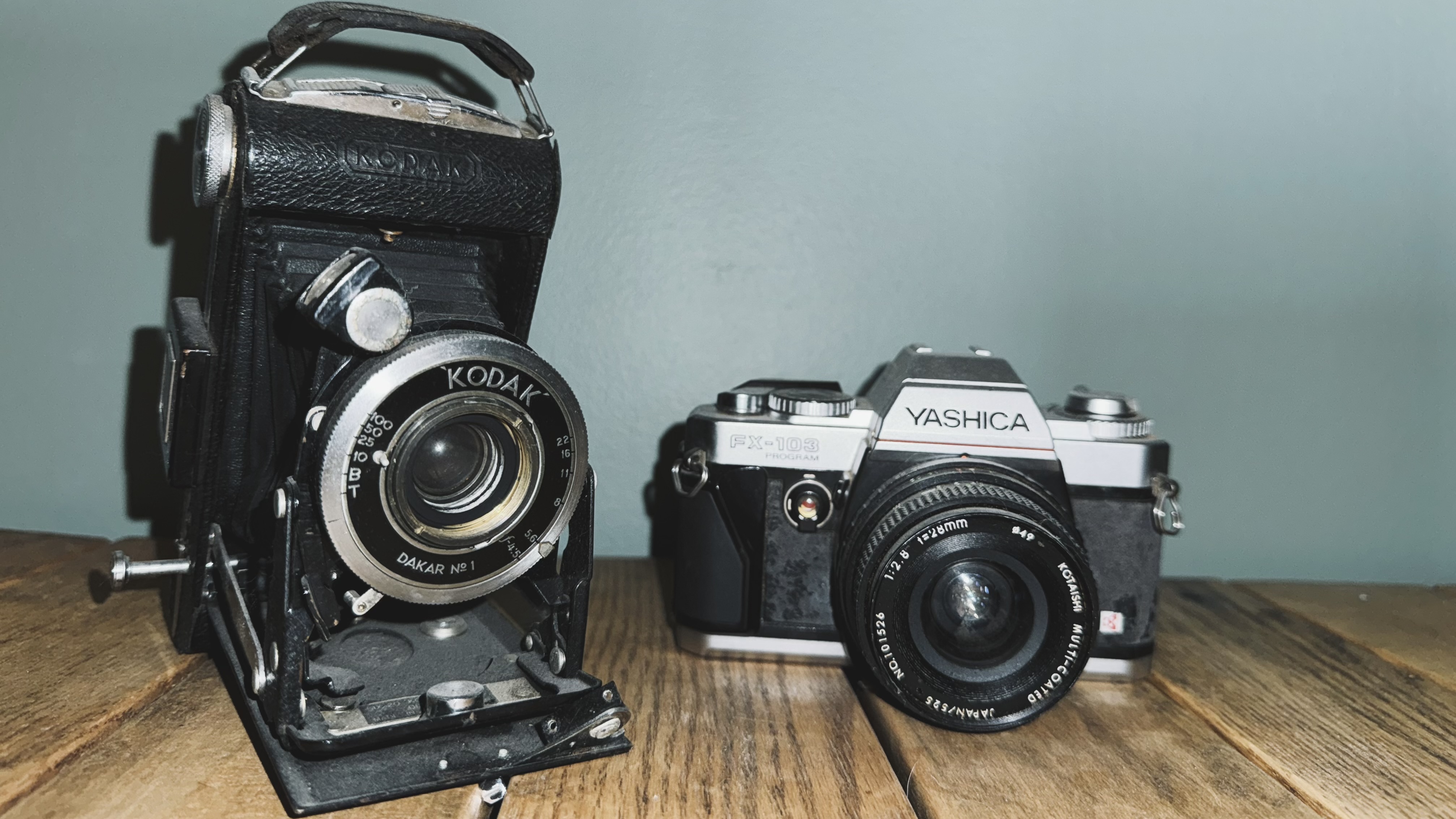 A pair of vintage cameras on a table with harsh direct flash shadows
