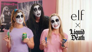 Three people wearing dramatic, black-and-white heavy metal face paint smile while holding up e.l.f. cosmetics tubes and Liquid Death beverage cans next to a promotional "e.l.f. x Liquid Death" logo.