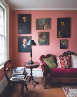 A bright pink living room with a gallery wall of unframed portraits and dark wood and velvet furniture.
