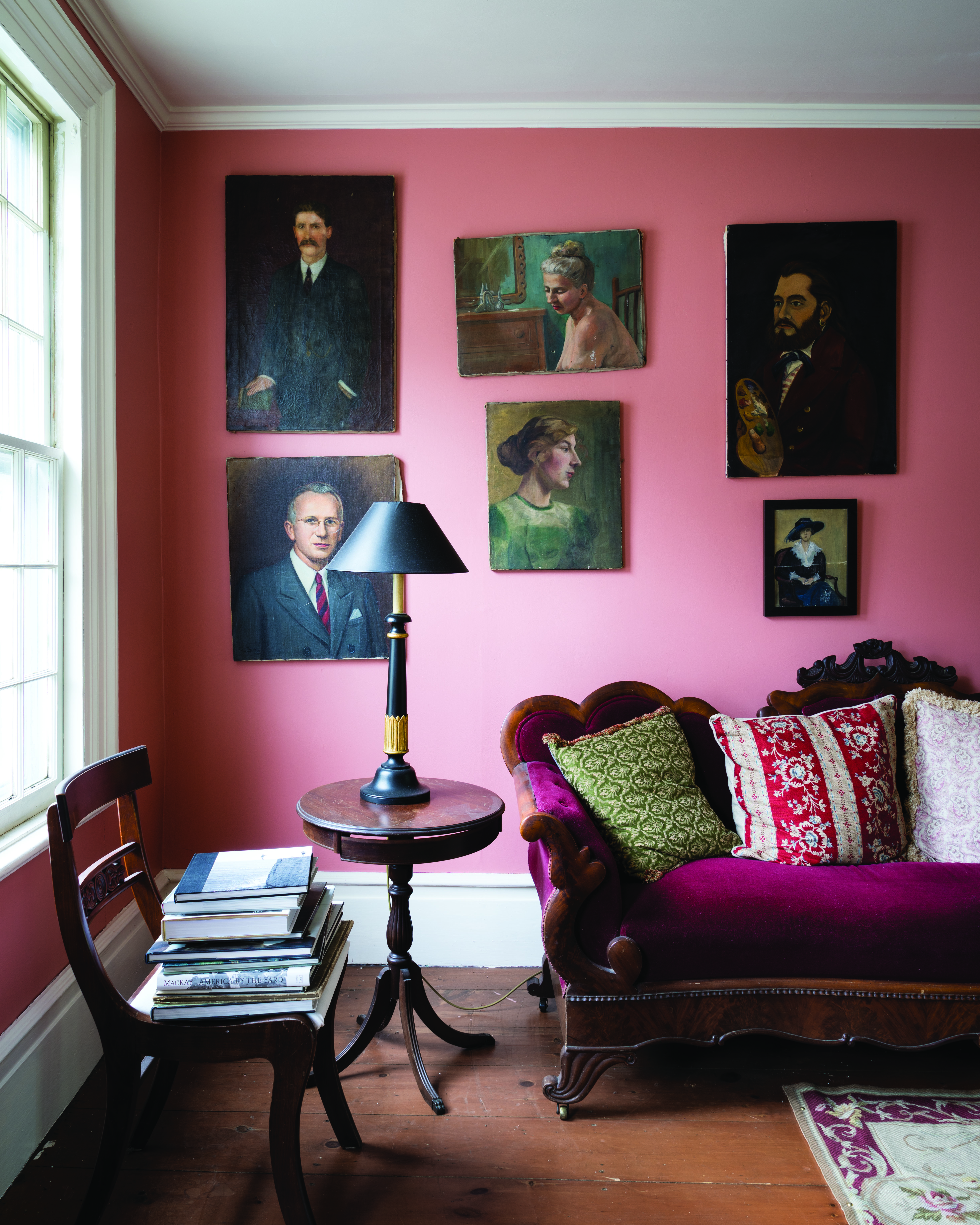 An eccentric example of small living room decor ideas showing a room with bright pink walls and a deep purple velvet couch.