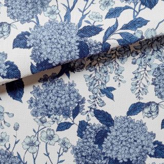 A square of white wallpaper with dark blue hygrangea illustrations on it and the top section of it folded