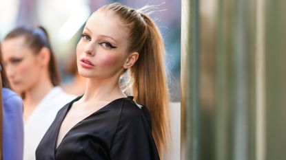 Sorina Stanciu wears winged eyeliner and a black lown-neck v-neck dress, during the Ramelle show, during "Feeric" Fashion Week 2021 In Sibiu, on July 23, 2021 in Sibiu, Romania. 