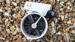 The DJI Flip drone, small in size and white in color, folded up with the propeller sitting underneath the body, on a stoney background.