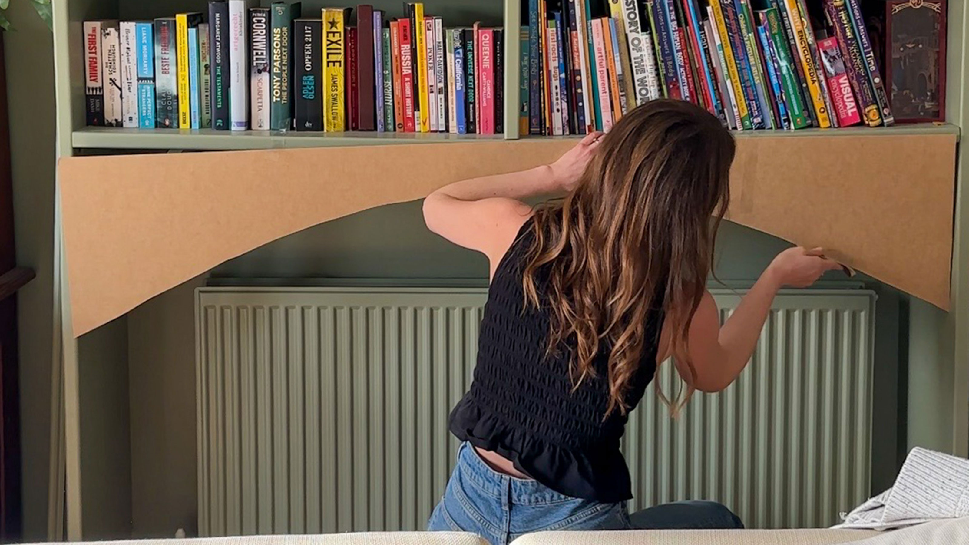 Woman adding plywood arch to bottom of green bookshelf above radiator