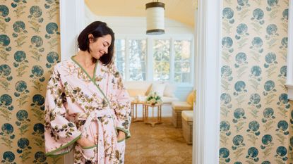 A model poses in a pink-and-green floral Weezie terry robe from the new Leah O'Connell collaboration inside a pattern-filled entryway