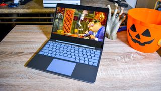 An open Surface Laptop Go sitting on a wooden desk, plastic jack'o lantern beside it