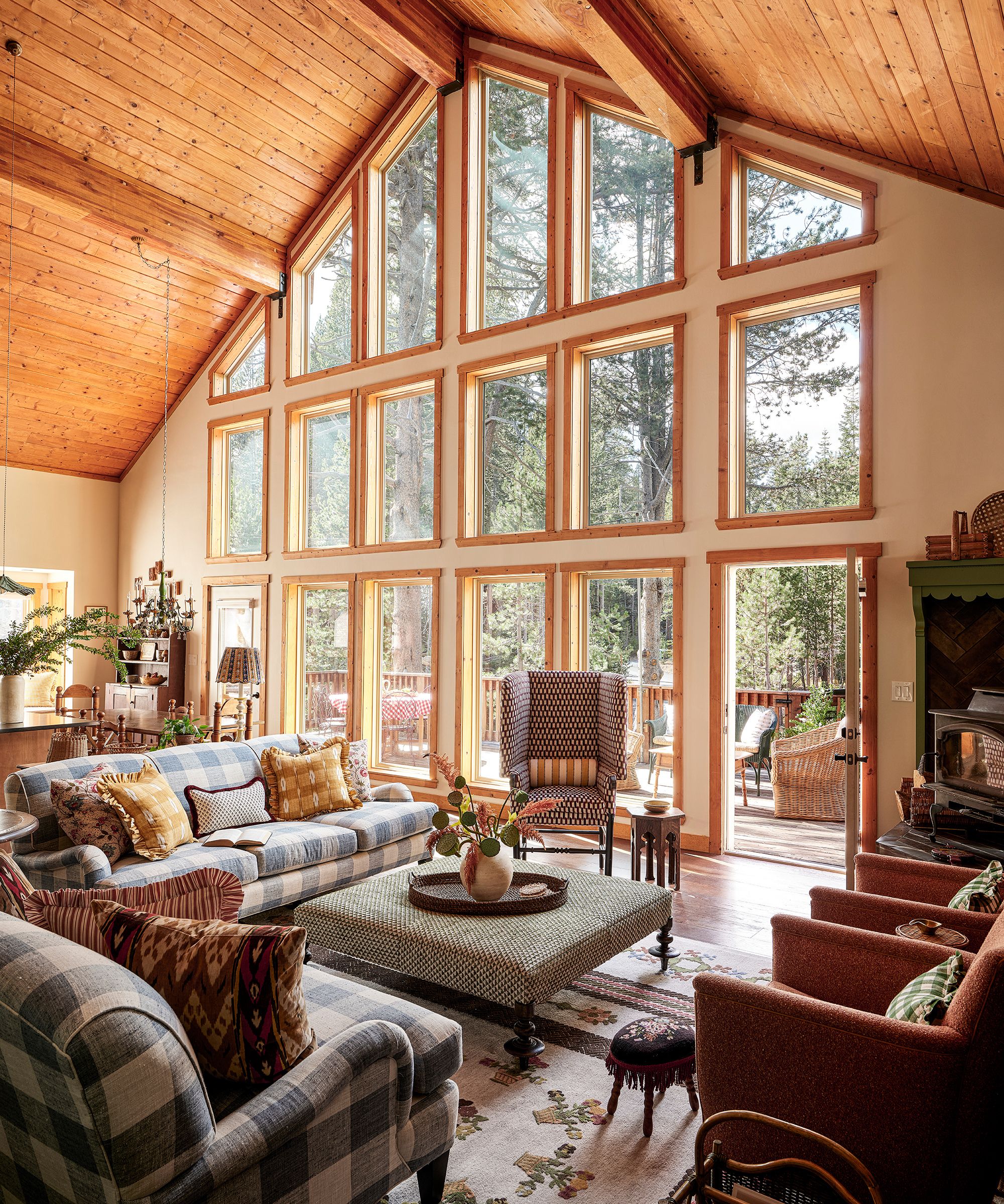 a vaulted ski chalet great room with large windows and a living room arranged around a stove, with blue gingham couches and a floral rug