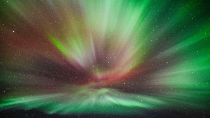 northern lights corona viewed directly overhead with long curtains of green and red light in the starry sky.
