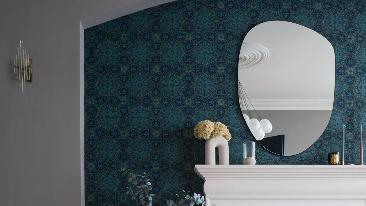 Living room with an asymmetric mirror above a fireplace and patterned wallpaper