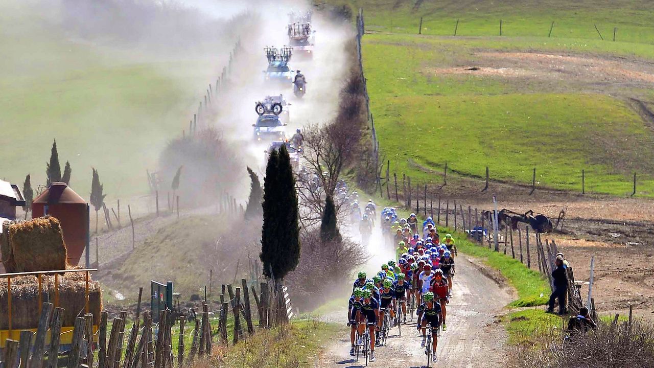 The peloton and race convoy kick up the white dust from the roads
