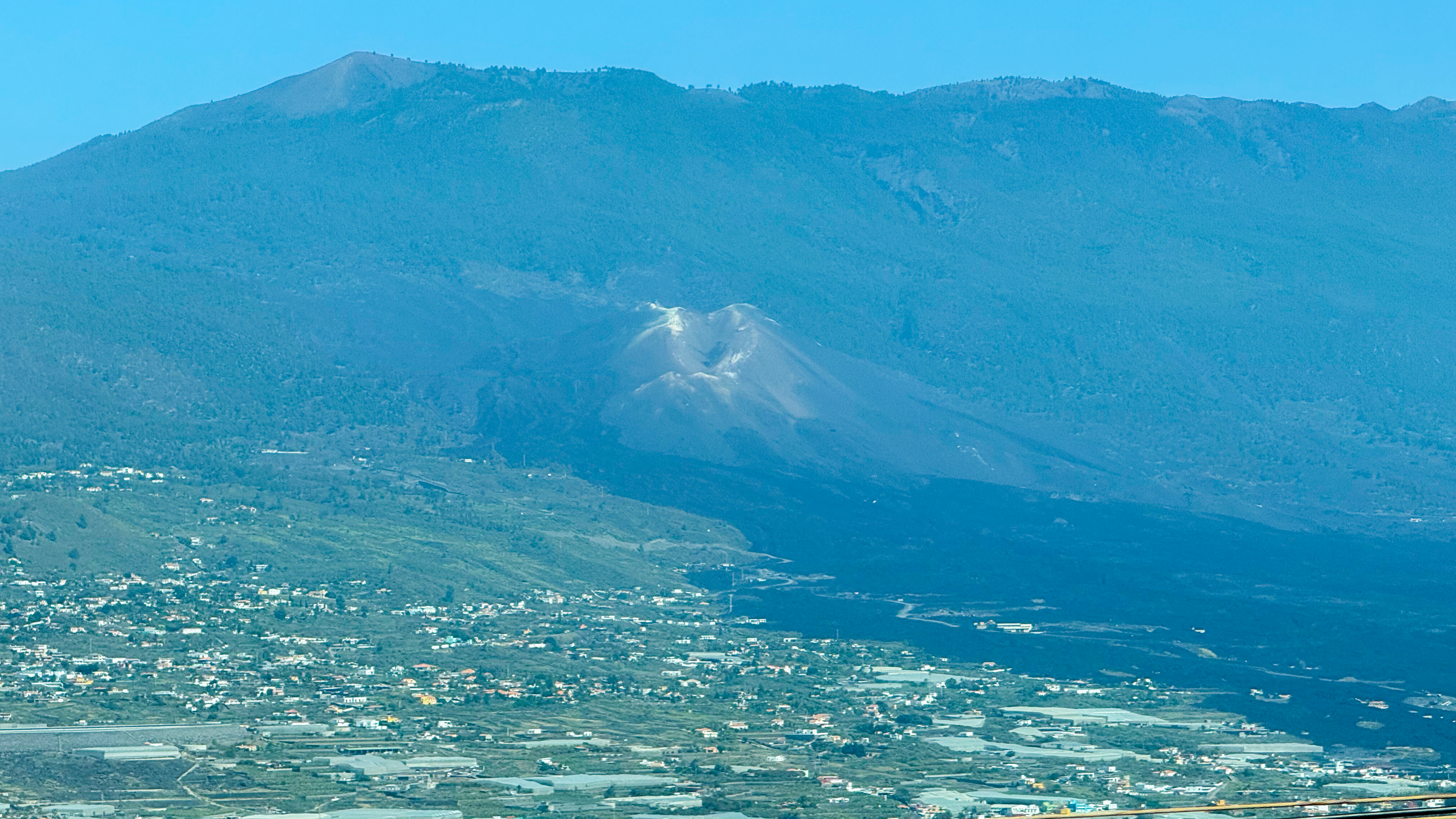 a volcano rising from the side of a mountain and a long flow of black rock - the lava field - visible against the lush green vegetation.