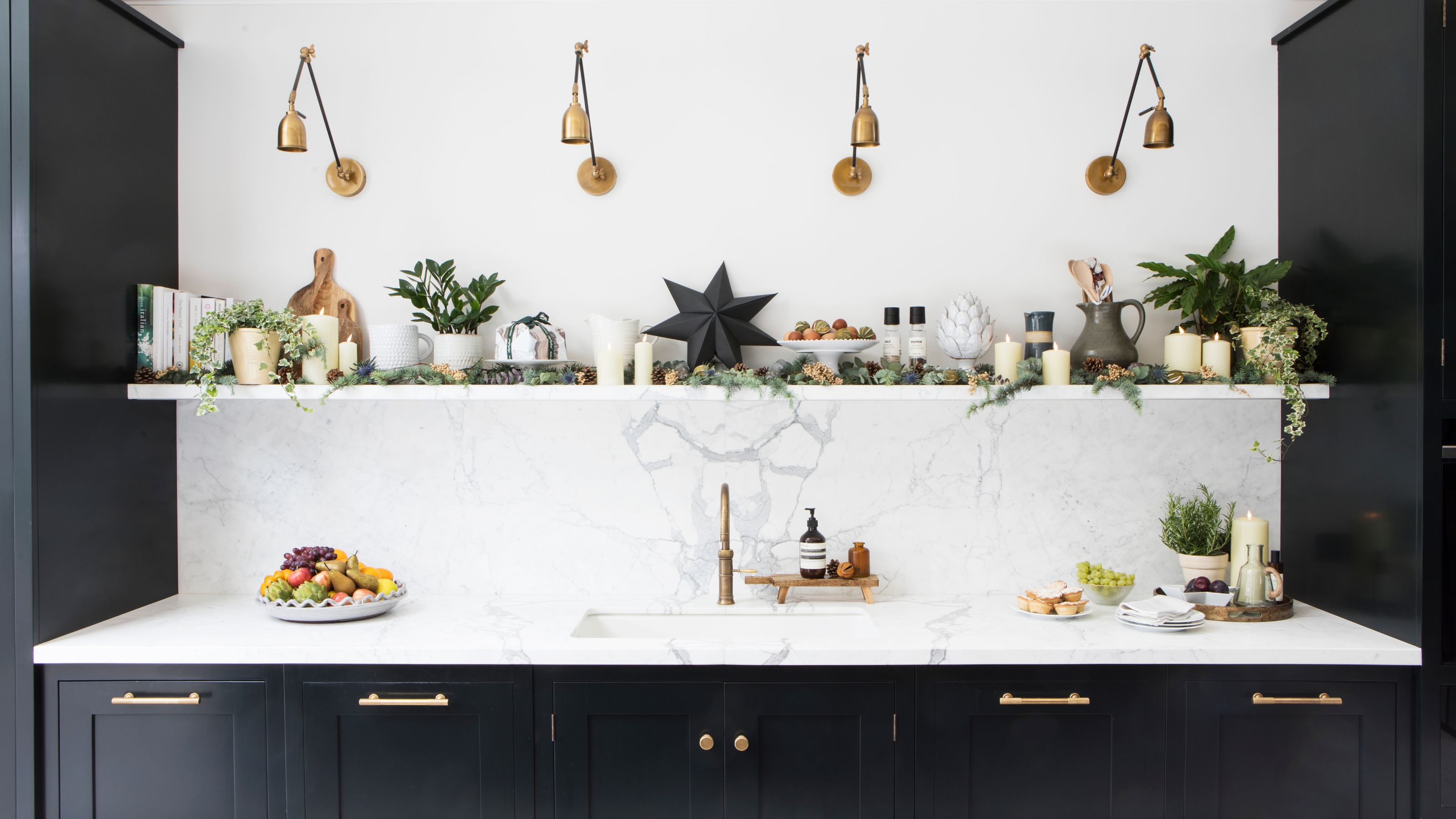 Kitchen sink area with white marble worktops, dark blue kitchen cupboards and a shelf with christmas decorations above