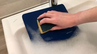 A mousepad being scrubbed with a sponge in the sink