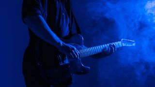 Guitarist plays music in neon light with smoke.
