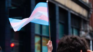 A hand holds up a small transgender pride flag during Bristol Trans Rights