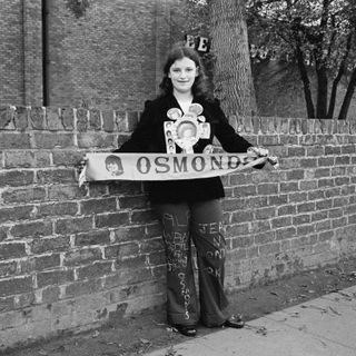 Girl wearing rosettes and holding banner saying The Osmonds