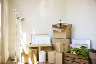 Stack of cardboard boxes with floor lamp in room. Moving objects against white wall.