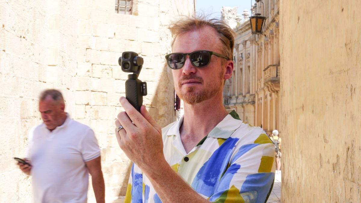 Man in bright summer short and shades, in an old town on a sunny day, holding the DJI Osmo Pocket 4P vlogging camera