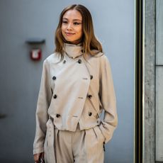 an attendee at milan fall winter 2025 fashion week wearing a short trench coat and trousers