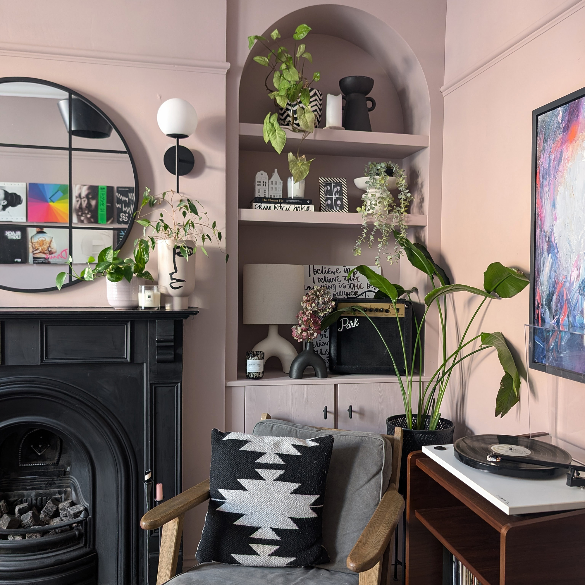 Soft pink living room with black fireplace and arched built-in shelves in the archive filled with decorative objects and plants