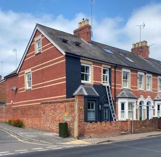 A brick house partially painted dark grey/black whilst the neighbouring houses are all red brick houses 