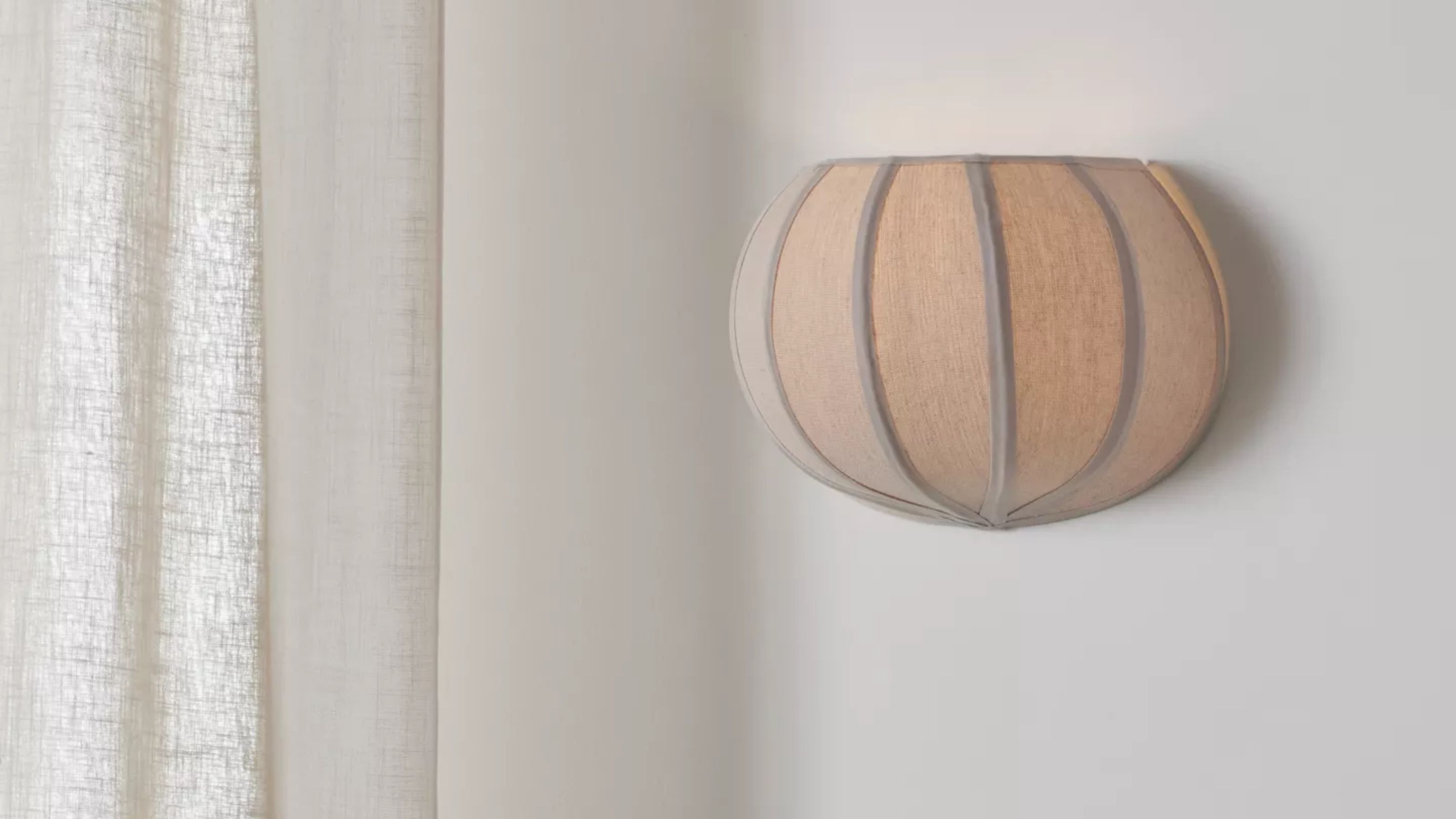 Image of a pumpkin-shaped wall sconce on a white wall next to a white linen curtain.