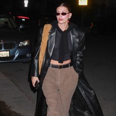 Hailey Bieber in a church outfit of a black crop top, suede pants, leather trench