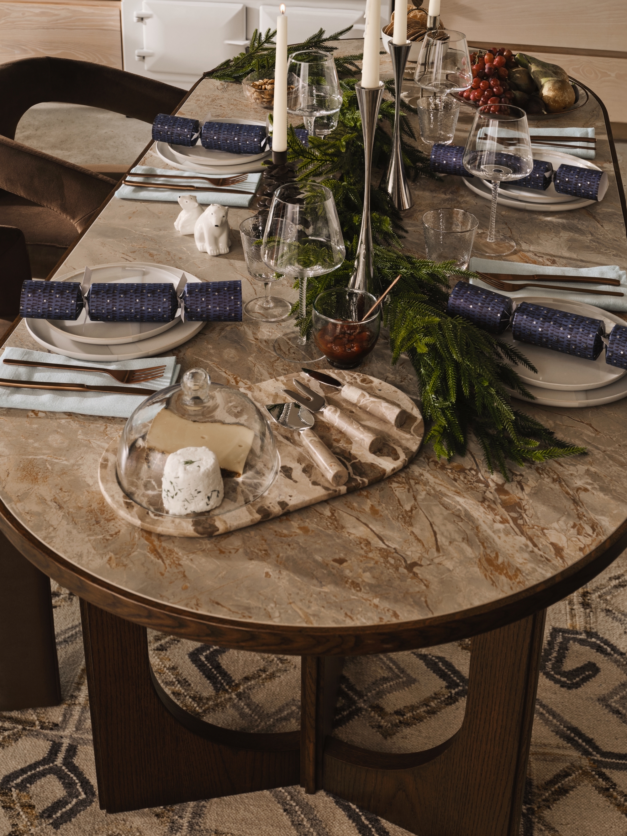 A dining table decorated for Christmas with chrome candle holders and a bough of foliage