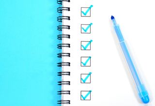 A blue notebook is open and a check list is written on the page with a blue pen.