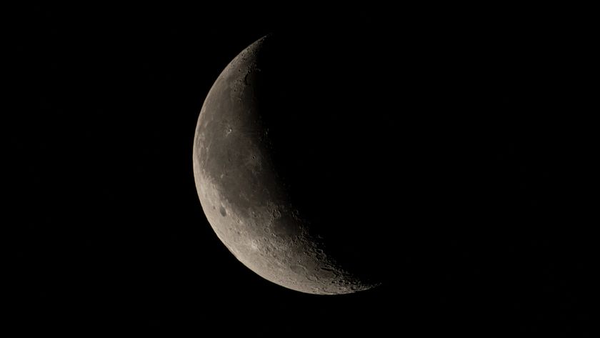 A close up of the moon in the darkness of space, with only a crescent shaped beam of light showing the surface