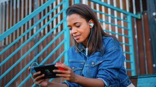 Bästa earbuds för gaming: En kvinna sitter utomhus i en trapp och använder ett par Turtle Beach Battle Bud-hörlurar och spelar på en Nintendo Switch.