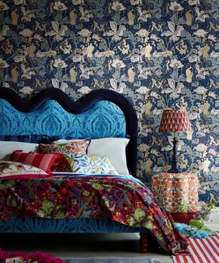 how to make a bedroom darker, colourful bedroom with patterned wallpaper, blue upholstered bed patterned throw and side table, lamp, rugs